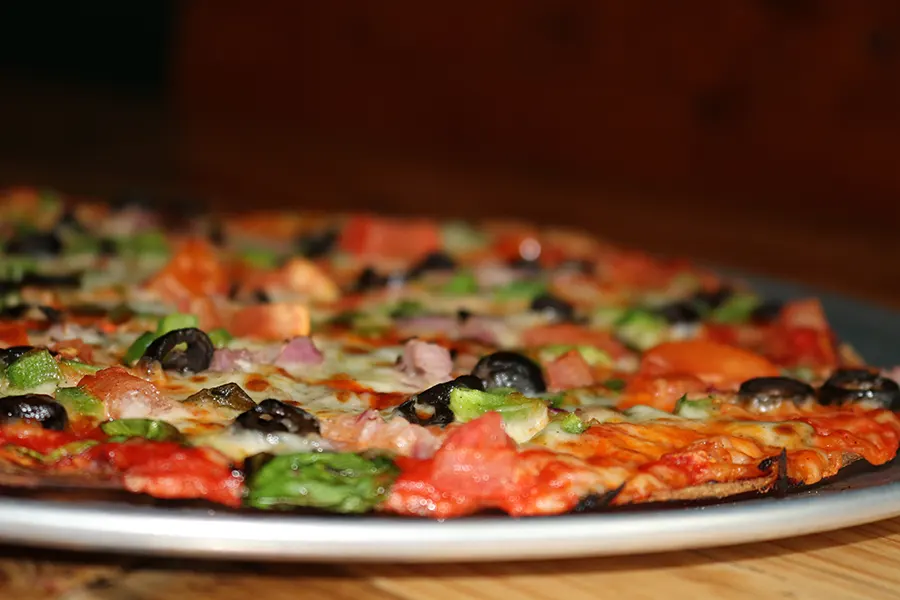 an extreme close-up of a delectable-looking thin-crust pizza loaded with toppings.